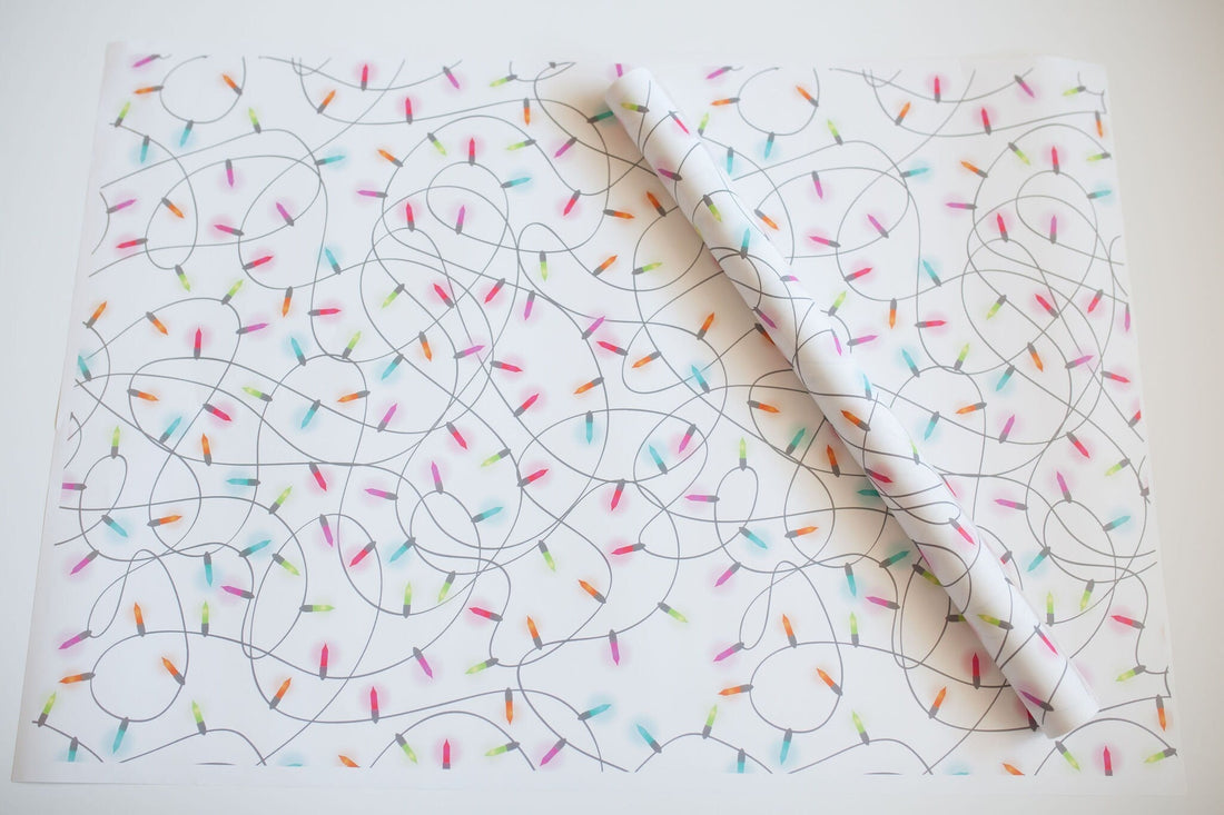 A White sheet of wrapping paper with Colorful Christmas Lights Tangled up and one rolled up sheet on top